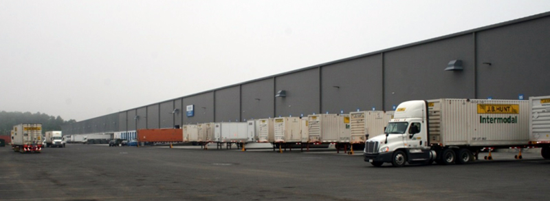 FIGURE 1. Newly Expanded Warehouse with More Than 100 Truck Loading Bays
This image shows truck trailers positioned at loading bays along the side of a modern warehouse. A tractor is attached to one trailer.

